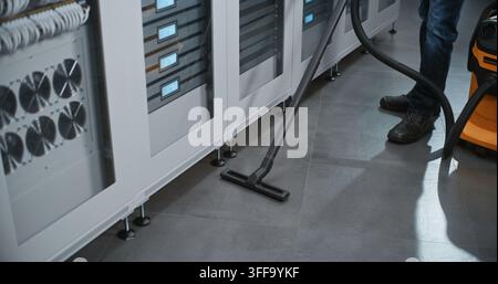 Technician Uses Heavy Duty Vacuum to Clean Tiled Aisle Between Rows of Server Cabinets. Facility Management and Cleanroom Maintenance Ensure Optimal Environmental Conditions For Enterprise Servers. Stock Photo