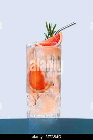 Refreshing cocktail with grapefruit, rosemary and ice in a glass on a blue background with shadow close up. Summer citrus drink or lemonade concept fo Stock Photo