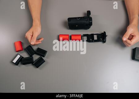 High-angle view of filmmaker loading rechargeable battery into black camera grip accessory, preparing for extended shooting sessions and enhanced vert Stock Photo