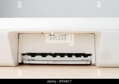 Close-up view of a white office printer showing the paper tray and output slot on a wooden desk, highlighting modern office equipment, minimal design Stock Photo