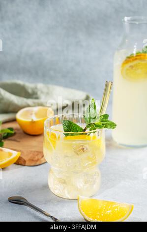 Fresh drink lemonade with lemon, mint and ice in glass on a light background with bottle and fresh herb and fruits. Summer trendy citrus mojito mockta Stock Photo