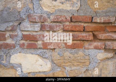 Weathered red bricks embedded in rough stone and mortar wall Stock Photo