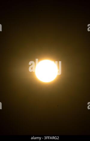 Bright sun disc floats in a smoky sky with subtle corona and faint lens haze suggesting high heat and drought as minimalist light dominates a quiet mo Stock Photo