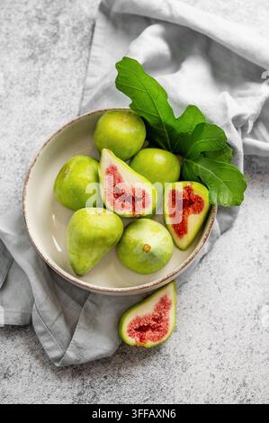 Sweet green figs in a plate with leaves and napkin on a gray concrete background. Concept of juicy and healthy summer fruits. Top view, copy space. Stock Photo