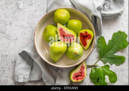 Sweet green figs in a plate with leaves and napkin on a gray concrete background. Concept of juicy and healthy summer fruits. Top view, copy space. Stock Photo