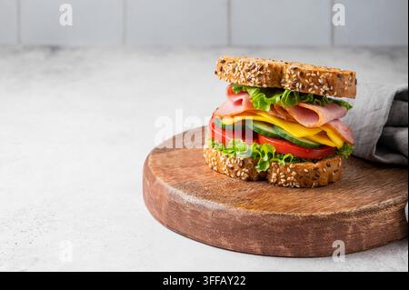 Sandwich with ham, cheese, lettuce and vegetable on a wooden board on a gray concrete background with napkin. Concept for a healthy, homemade snack fo Stock Photo
