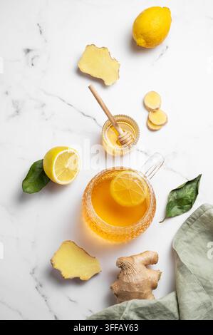Flat lay of a glass cup of hot tea with fresh lemon and ginger on a light marble background with honey, citrus fruits, root and napkin. Concept of a n Stock Photo