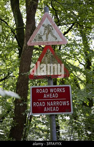 Weathered and moss-covered road signs warning of road works and narrowing roads on Longshaw Ford Road in Bolton, Greater Manchester, UK. Stock Photo