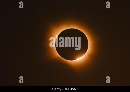 A total solar eclipse showing glowing golden corona rays around the moon silhouette with a chain of bright Baily's beads shining along the lower edge Stock Photo