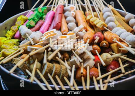 Close-up of assorted sausage, fish ball and fish cake skewers piled on a round metal tray at a Bangkok street food market, Thailand Stock Photo