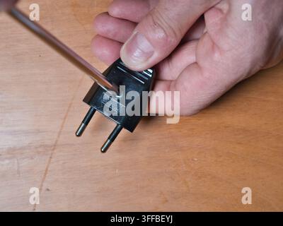 Hand Wiring Electrical Plug with Screwdr - A close-up shot of a person's hand using a screwdriver to connect wires inside a disassembled electrical pl Stock Photo