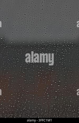 Raindrops on window glass during dark overcast storm. Stock Photo