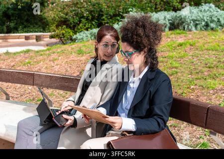 Businesswomen collaborating and discussing work on a park bench Stock Photo