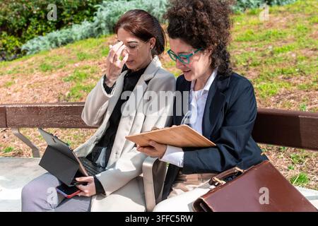 Businesswomen collaborating on laptop and clipboard outdoors working Stock Photo