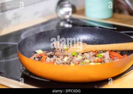 Raw ground beef being fried in a pan with cooking oil and wooden spoon during preparation of a fresh high protein meal Stock Photo