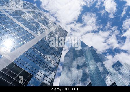 A low angle view of modern glass skyscrapers reflecting a bright blue sky with scattered white clouds. Stock Photo