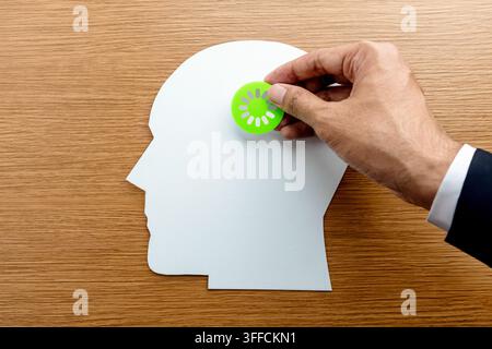 Businessman hand placing a green loading icon onto a paper human head. Corporate burnout, mental fatigue, slow cognitive processing concept. Stock Photo