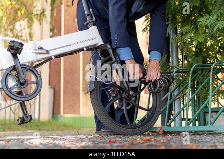 businessman take his bicycle from parking. A new modern alternative mode of transport. Eco-friendly electric bike. An employee in a suit is strapping Stock Photo