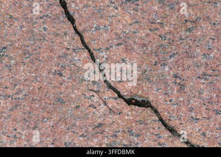 Close-up of a pink granite paving surface with a prominent dark crack running across the textured stone  Tags Stock Photo