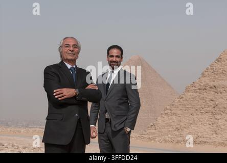 Two multigenerational Middle Eastern male executives in formal business suits posing with authority before the monumental Giza pyramids ideal for MENA Stock Photo