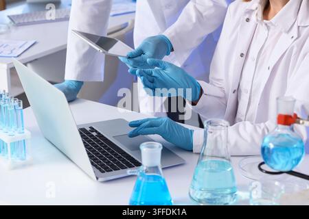 Medical research and scientific innovation, scientists using laptop and tablet for data analysis in laboratory with chemical glassware and blue liquid Stock Photo