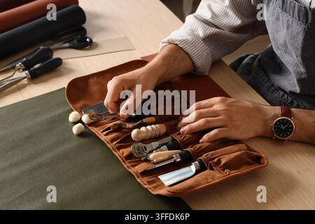 Leather craft and artisan workshop, skilled craftsman working with professional tools and leather materials at a wooden workbench in a creative studio Stock Photo