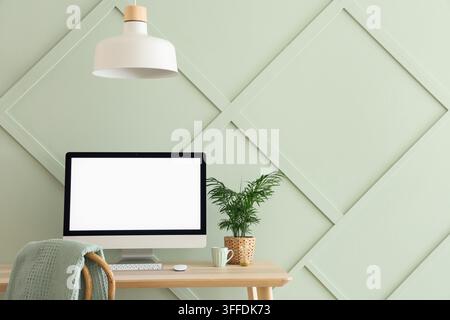 Remote work and home office setup, computer with blank screen for mockup on wooden desk in modern interior with green wall and minimalist decor Stock Photo