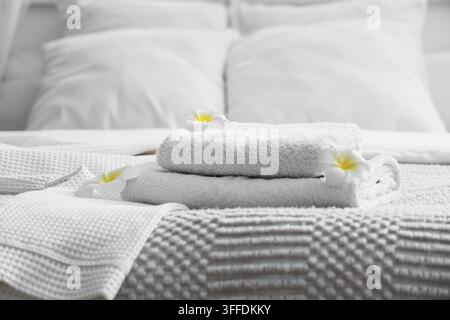 Clean towels with bathrobe and plumeria flowers on bed in hotel room, closeup Stock Photo