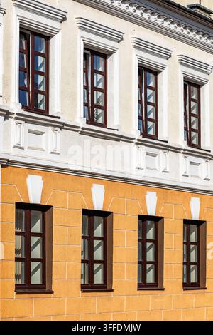 Two story building facade with dark wooden windows, white decorative trim, and yellow plaster wall. Elegant classical architectural style featuring fr Stock Photo