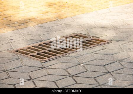 Rectangular cast iron drainage grate installed in a paved sidewalk surface. Heavy duty street gutter grate designed for effective urban storm water ma Stock Photo