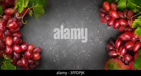 Gorgeous red grapes with green beautiful leaves on a gray board as an elegant background for everything to do with wine Stock Photo