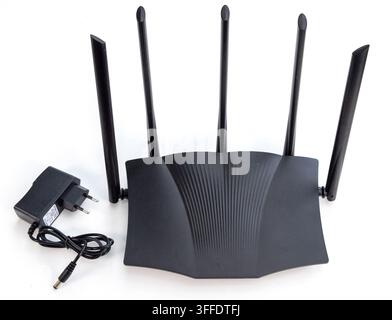A black WiFi router with four antennas and power adapter rests on white Stock Photo
