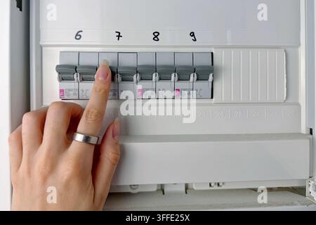 Close-up of a hand checking circuit breakers in a residential electrical distribution panel with multiple labeled switches and protective devices Stock Photo