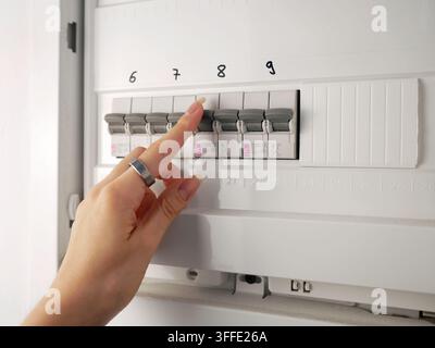 A hand checking circuit breakers in a residential electrical distribution panel with multiple labeled switches and protective devices Stock Photo