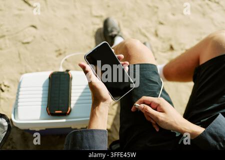 Man Charging Smartphone with Portable Solar Power Bank Outdoors Stock Photo
