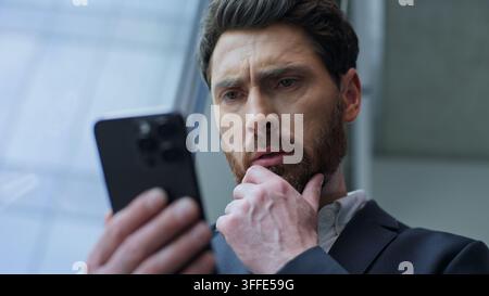 Pensive worried Caucasian business man thinking with mobile phone looking out window in office middle-aged 40s businessman anxiety male executive Stock Photo