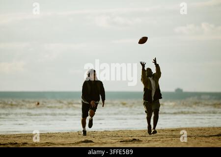 Multiethnic Friends Playing American Football on Beach Stock Photo