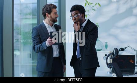 Two multiracial business men communicating about startup holding at digital tablet in corporate office Caucasian and African American businessmen Stock Photo