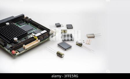 A circuit board is placed on a table with various electronic parts spread around it. The components include chips, capacitors, and resistors. Stock Photo