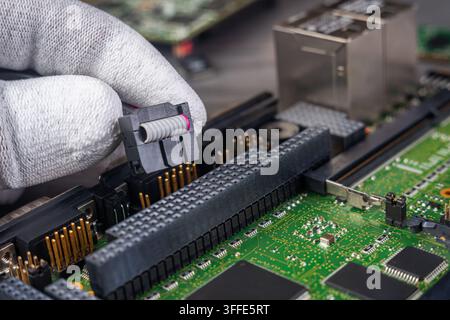 A technician holds a component while fixing a circuit board in an electronics workshop. Tools and other boards are visible on the table. Stock Photo