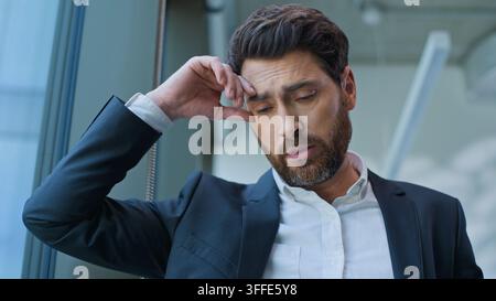 Caucasian middle-aged business man male employer sad leaning at window think in office pensive worried frustrated European anxiety manager executive Stock Photo