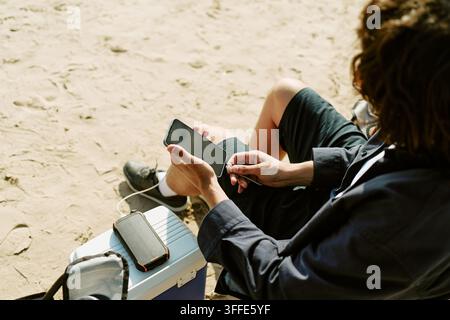 Man Charging Smartphone with Portable Power Bank on Beach Stock Photo