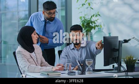 Two indian business colleagues talking working with computer leader coming check work help give advice for work result. Muslim three workers team talk Stock Photo