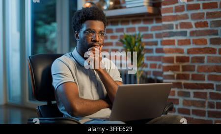 Pensive African American business man thinking coming up with idea working laptop at evening office troubled businessman male guy manager professional Stock Photo