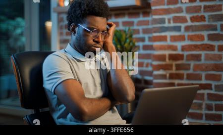 Worried anxious African American business man thinking looking at laptop at evening office pensive troubled businessman male guy manager professional Stock Photo