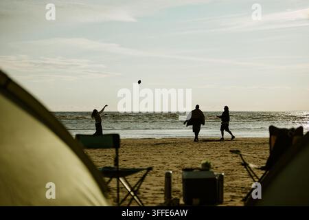 Friends Playing with Ball on Beach during Camping Trip Stock Photo