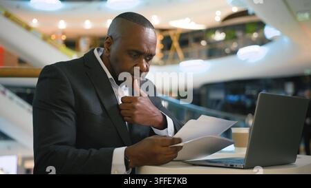 Middle-aged pensive African American business man working with papers and laptop thinking businessman male entrepreneur executive work with documents Stock Photo
