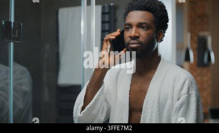 Serious African American man confident talking mobile phone looking mirror reflection at home bathroom guy talk smartphone call communicating chat at Stock Photo