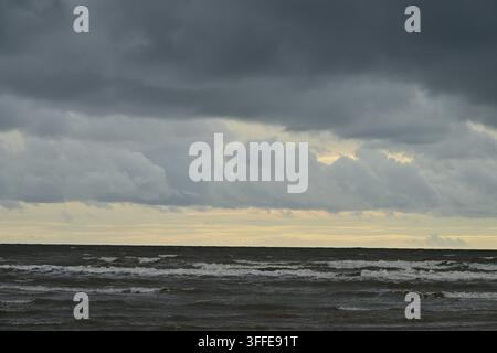 Overcast seascape with small breaking waves and faint yellow horizon glow visible Stock Photo