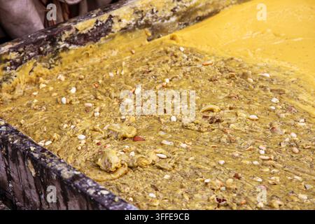 View of traditional jaggery being prepared in a large wooden container, mixed with nuts and seeds in Multan, Punjab, Pakistan. Stock Photo